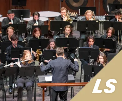 A man conducting a group of students playing woodwind and brass instrument during a concert.