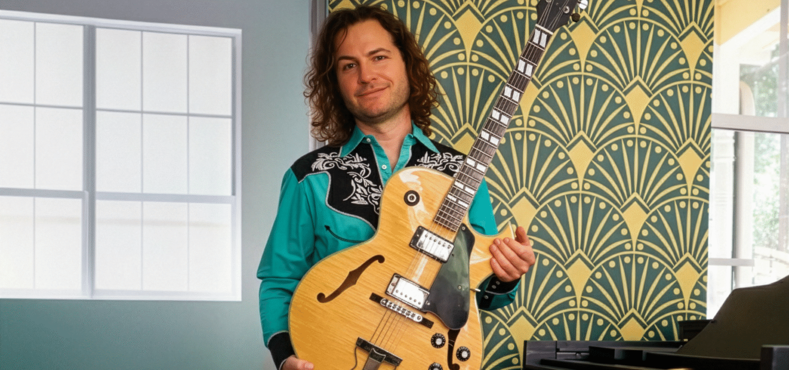 Man standing near piano holding guitar