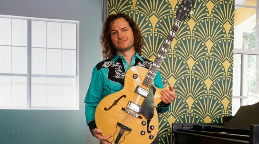 Man standing near piano holding guitar