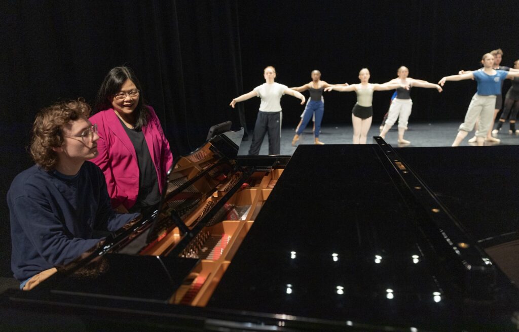 Teacher and student at piano, dancers in background