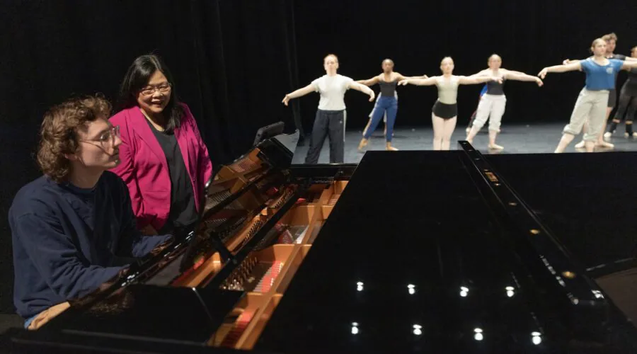 Teacher and student at piano, dancers in background