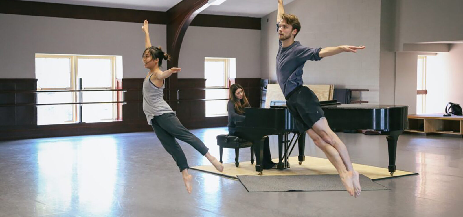 Two dancers mid-leap, pianist in background
