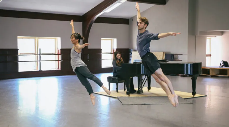 Two dancers mid-leap, pianist in background