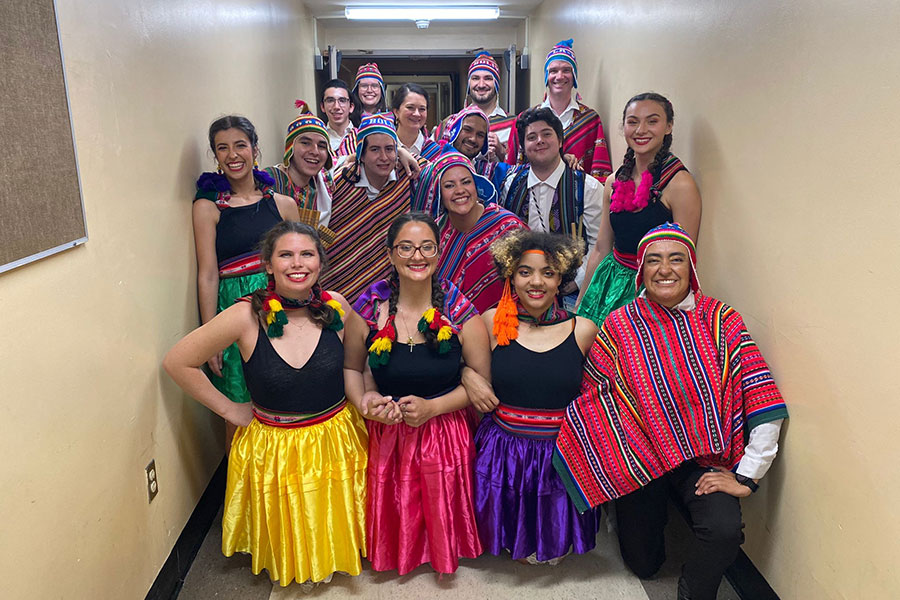 Group of smiling young men and women in brightly colored costumes posing for photo in hallway