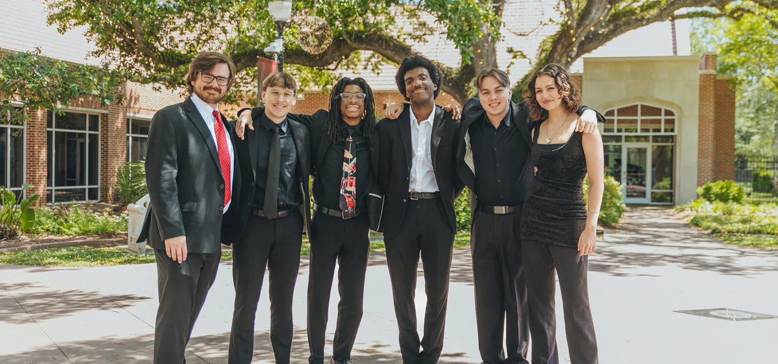 Group of smiling students standing in courtyard with arms around each other's shoulders