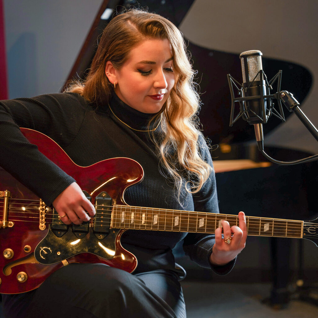 Young woman playing electric guitar in studio