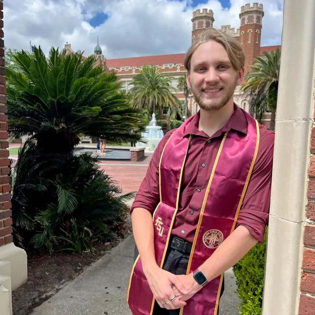 Photo of smiling young man leaning against stone arch with Westcott fountain and building in background