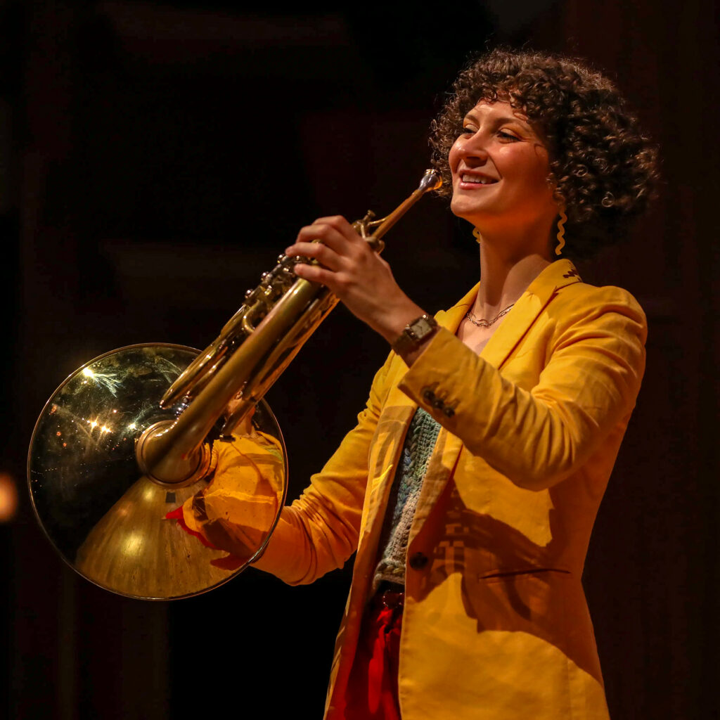 Smiling young woman holding French horn on stage