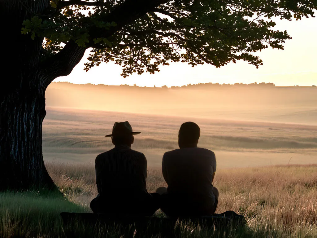 Silhouettes of two men sitting under a tree in an empty field