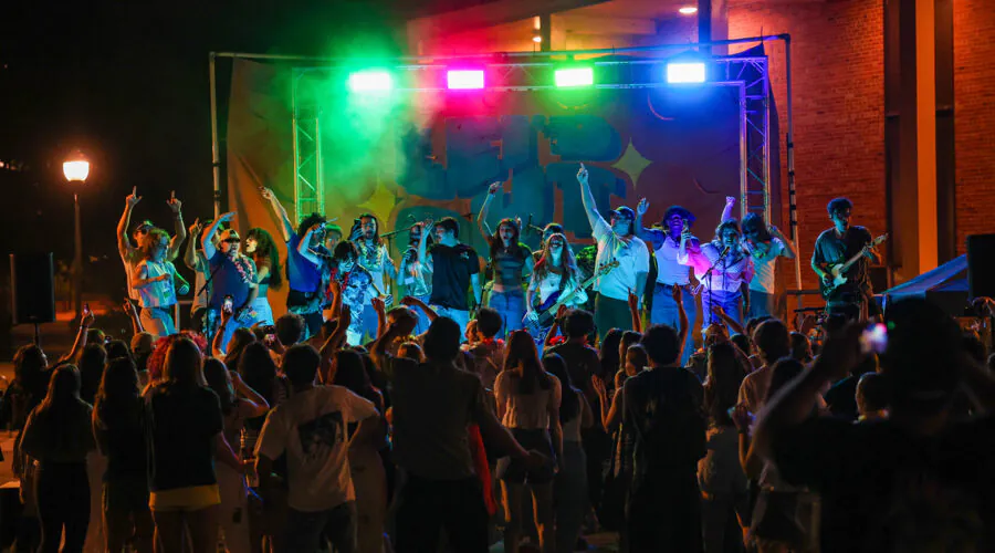 Performers and audience during nighttime concert, stage lit with colorful lights