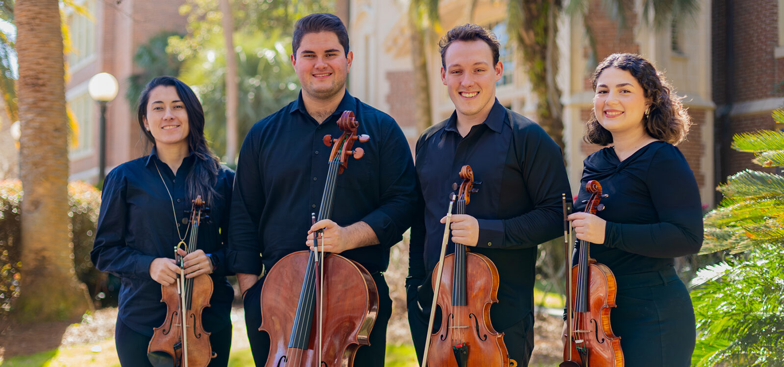 Quartet members holding instruments outside a brick building