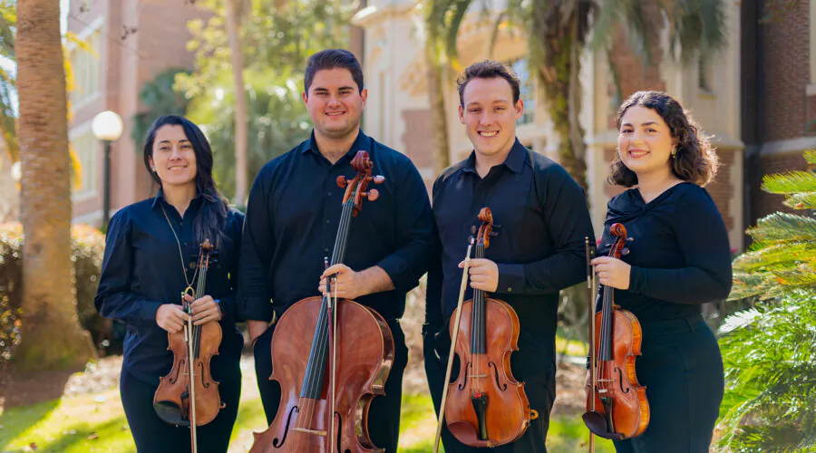 Quartet members holding instruments outside a brick building
