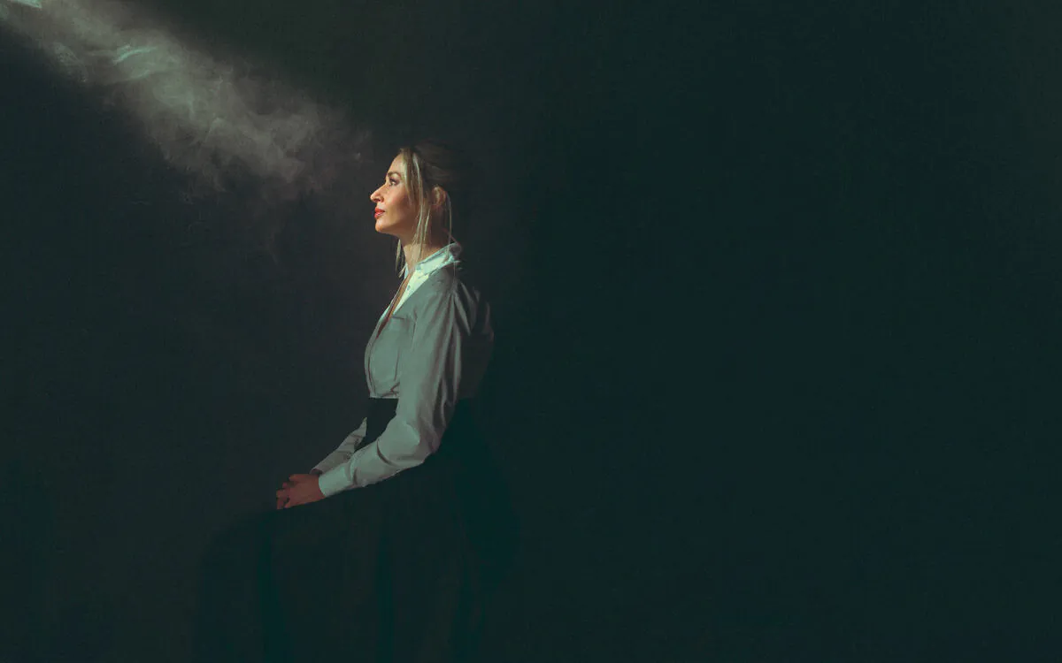 Woman seated in dark room facing into ray of light