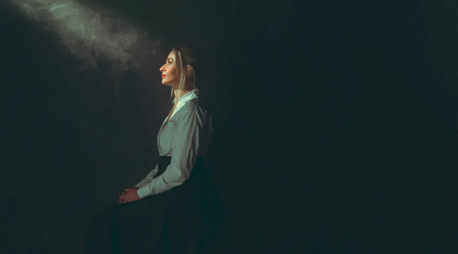 Woman seated in dark room facing into ray of light