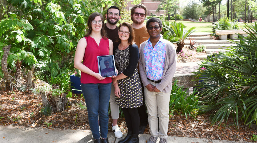 Four students and their professor posing for an outdoor photo