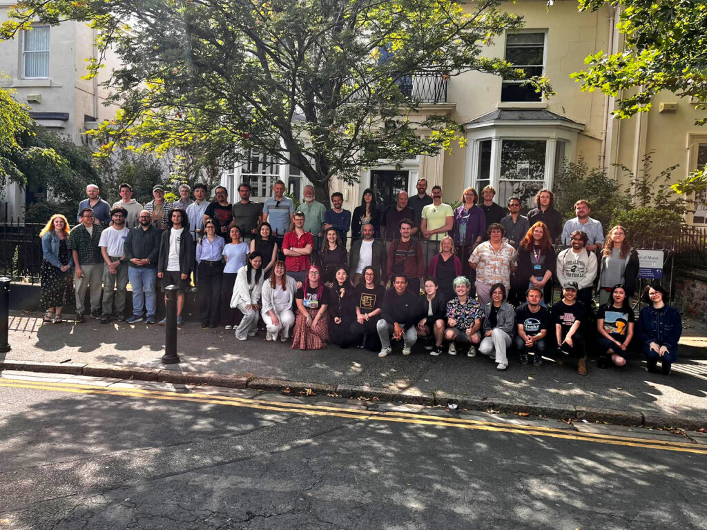 Large group of people posing for photo on sidewalk in front of yellow house