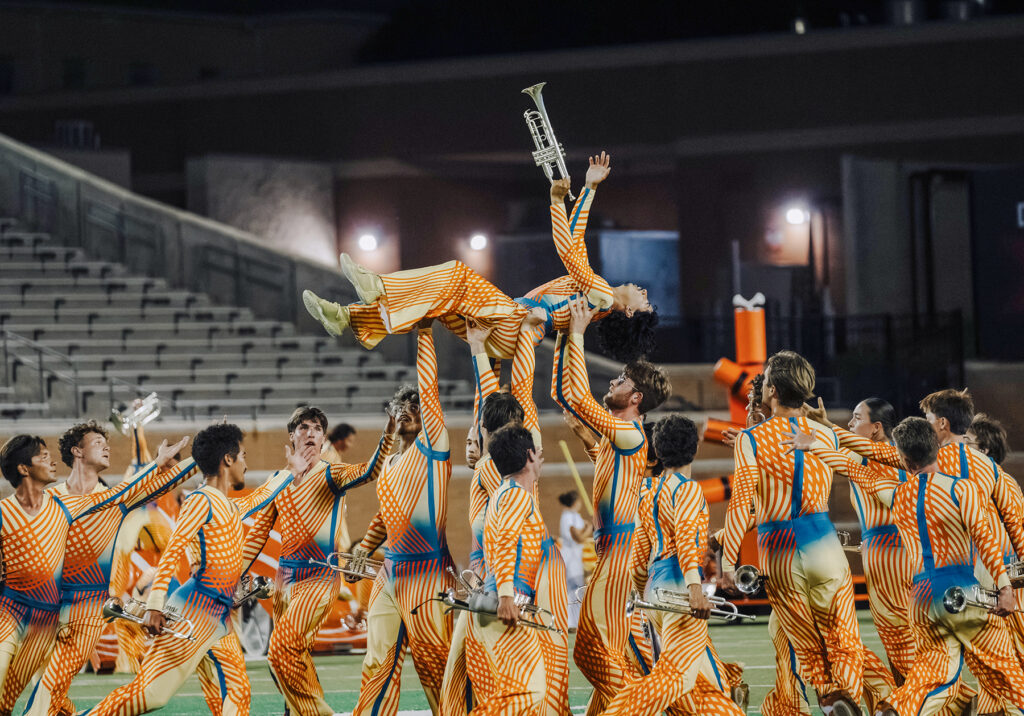 Young man with trumpet lifted above other trumpet players as part of a marching band drill