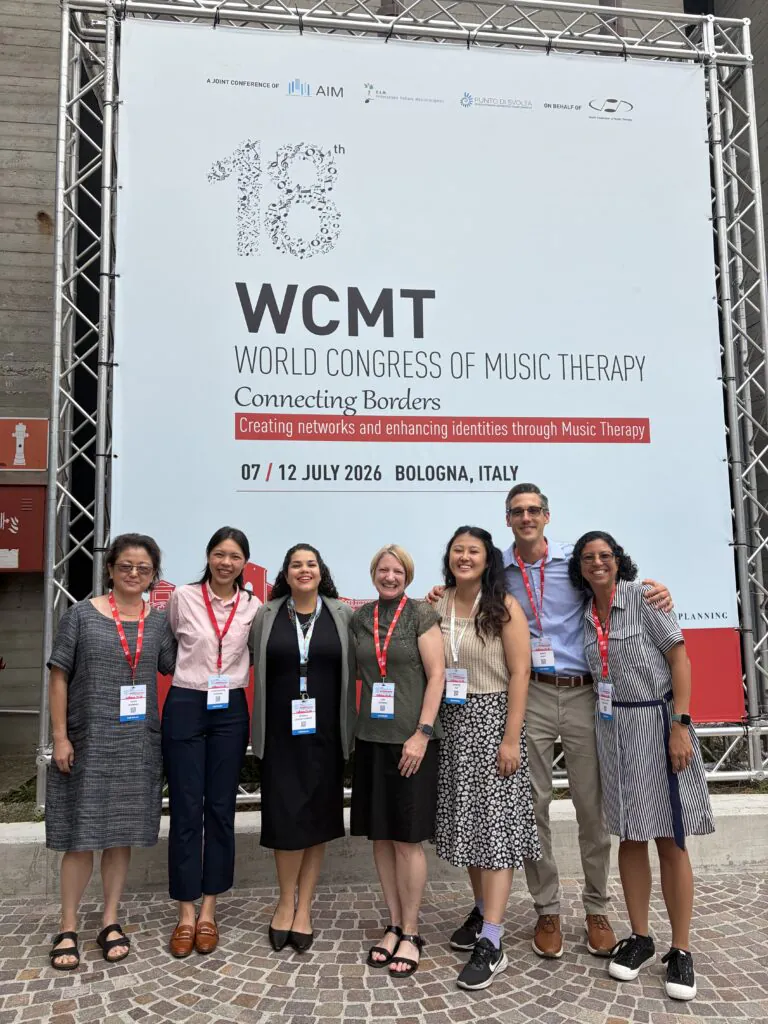 Six women and one man posing for photo in front of large sign
