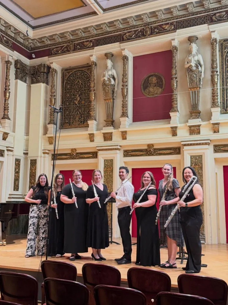 Group of students holding flutes posing with teacher in a performance space