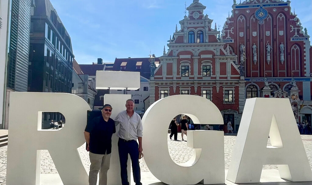 Two men standing in front of "RIGA" sculpture in an outdoor courtyard
