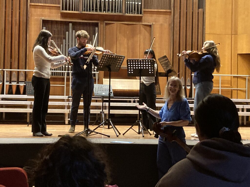 smiling woman gesturing at group of string players on stage