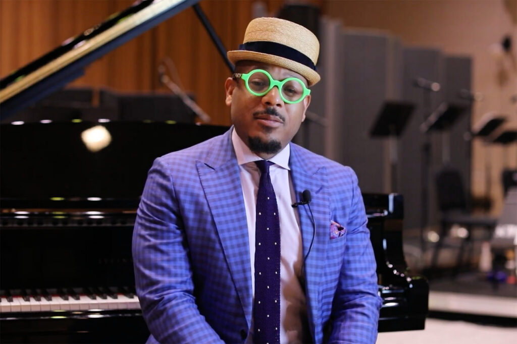 Man in hat and glasses seated at piano