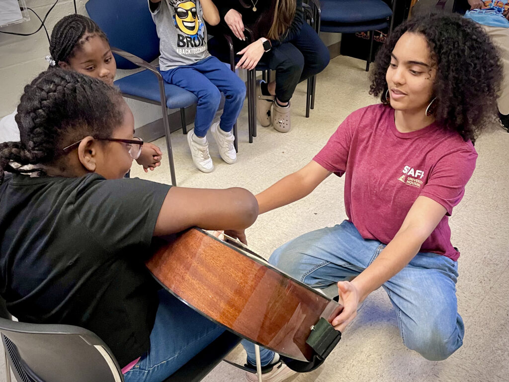 College student positions guitar for younger child