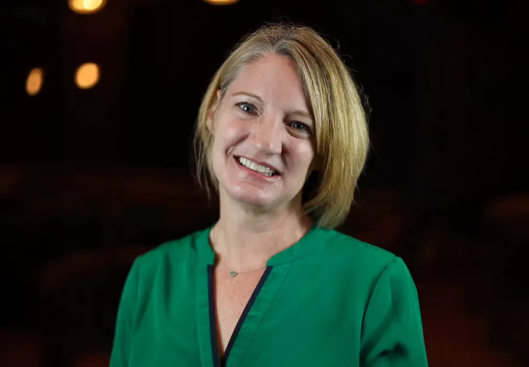 Blonde woman in darkened hall, smiling at camera