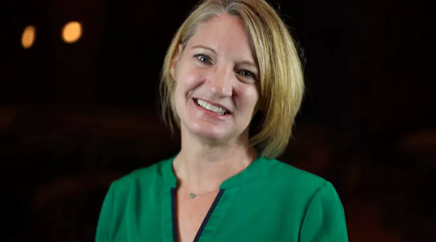 Blonde woman in darkened hall, smiling at camera