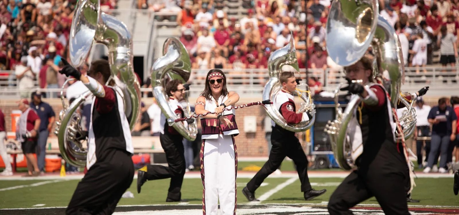 drum major on field surrounded by Sousaphones