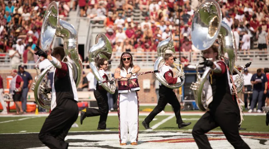 drum major on field surrounded by Sousaphones