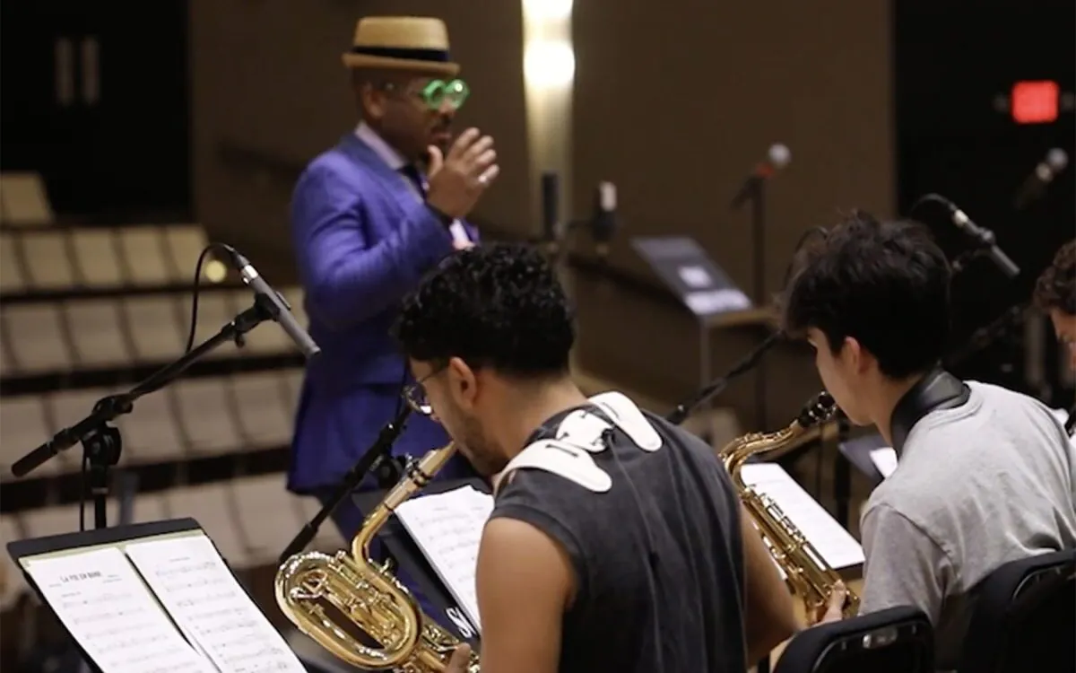 seated students playing saxophone, conductor out of focus in background