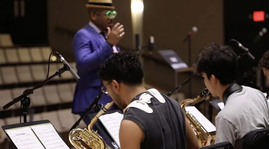 seated students playing saxophone, conductor out of focus in background