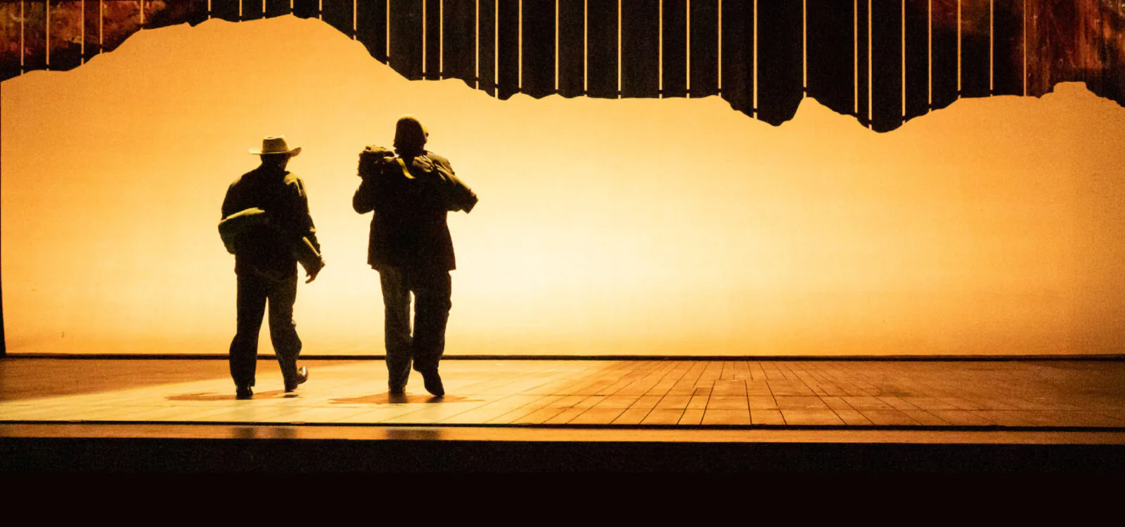 silhouette of two men walking toward back of lighted stage