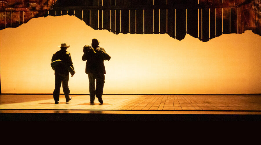 silhouette of two men walking toward back of lighted stage